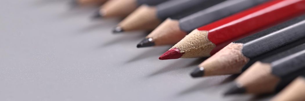 Closeup of one red wooden pencil among many black background. Distinctive personality traits concept