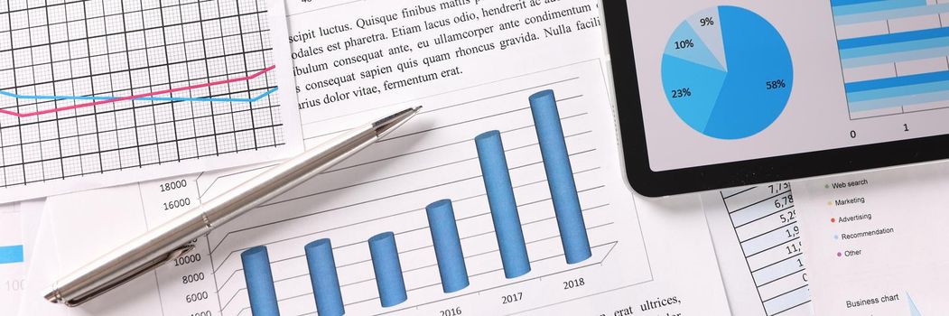 Digital tablet and papers with charts and diagrams lying on desktop closeup. Growth of statistical indicators concept