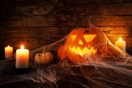 Festive mystical halloween interior. Pumpkin, spider web, burning candles, spiders on dark wooden background