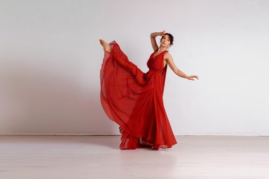 Dancer in a red flying dress. Woman ballerina dancing on a white studio background.