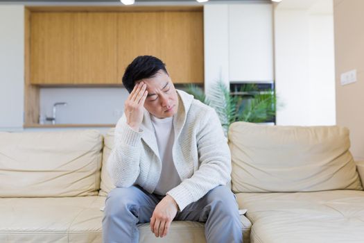 young asian man sitting on sofa at home pensive, worried about problems and depression. male has an experience relationships at work or family, problems with loan repayment debt Seriously conceived