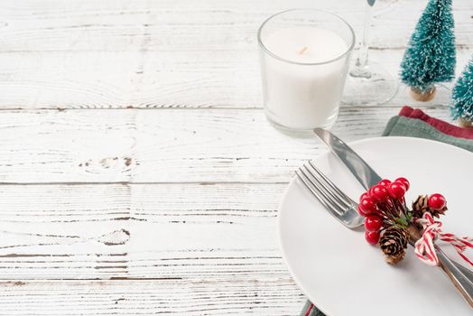 Christmas table setting with white dishware, silverware and red and green decorations on white wooden background. Top view, flat lay copy space