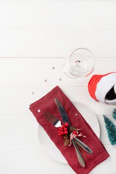 Christmas table setting with white dishware, silverware and red and green decorations on white wooden background. Top view, flat lay copy space