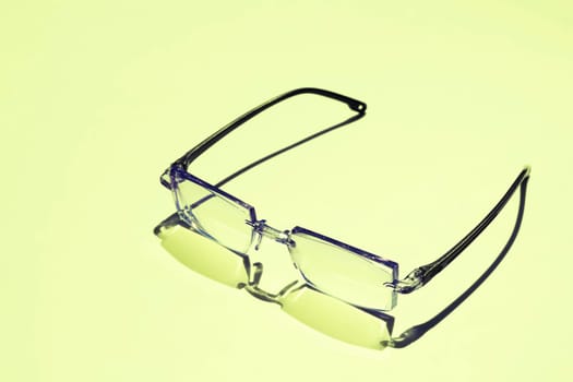 a pair of lenses set in a frame resting on the nose and ears, used to correct or assist defective eyesight or protect the eyes. Black framed eyeglasses on yellow background