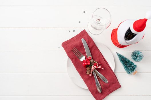 Christmas table setting with white dishware, silverware and red and green decorations on white wooden background. Top view, flat lay copy space