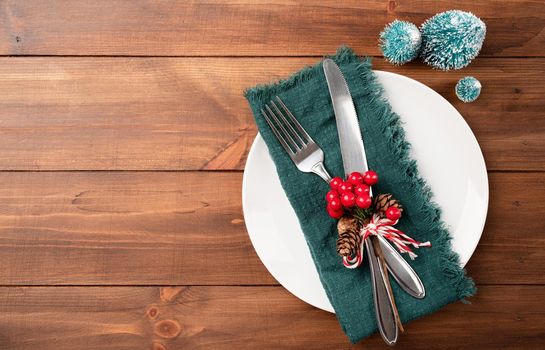 Christmas table setting with white dishware, silverware and green decorations on wooden background. Top view, flat lay