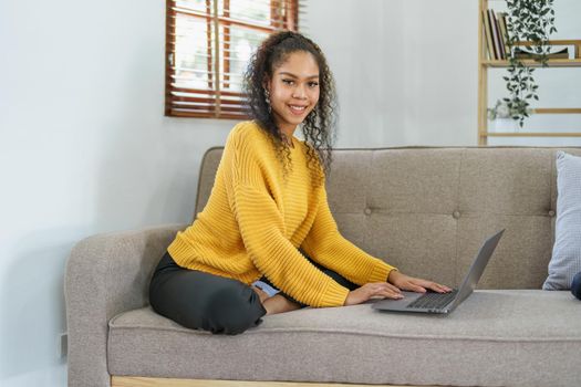 Portrait of an African American sitting on the sofa wearing on-ear headphones and using a computer at home.