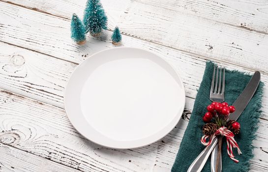 Christmas table setting with white dishware, silverware and red and green decorations on white wooden background high angle view