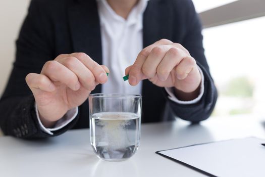 Close up of businessman in the office holding pills and glass of fresh water, taking medicine for headache, abdominal pain or taking vitamins, healthcare concept