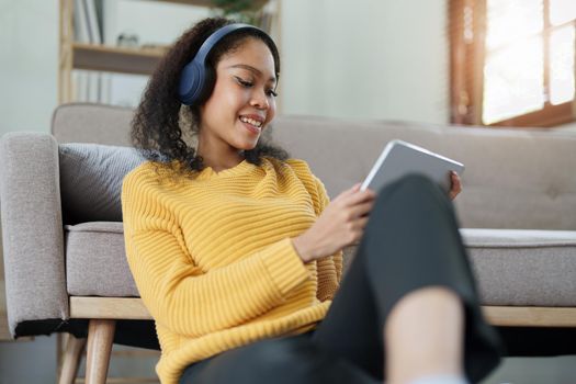 Portrait of an African American with headphones and tablet smiling happily listen music while relaxing on the sofa at home.