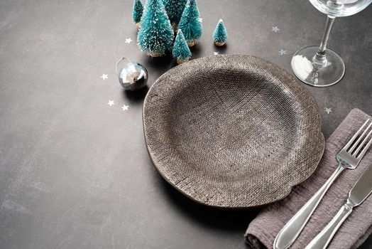 Christmas table setting with black dishware, silverware and green decorations on dark background. Top view flat lay