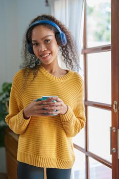 African American wearing headphones and holding coffee mugs smiling happily while listening to music relaxing at home