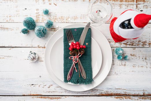 Christmas table setting with white dishware, silverware and red and green decorations on white wooden background. Top view, flat lay