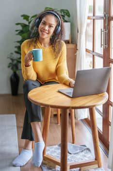Portrait of an African American wearing headphones holding a coffee cup and using a computer.