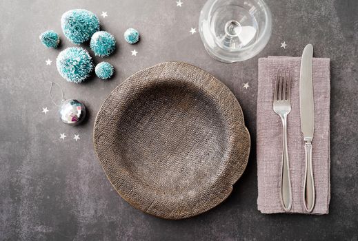 Christmas table setting with black dishware, silverware and green decorations on dark background. Top view flat lay