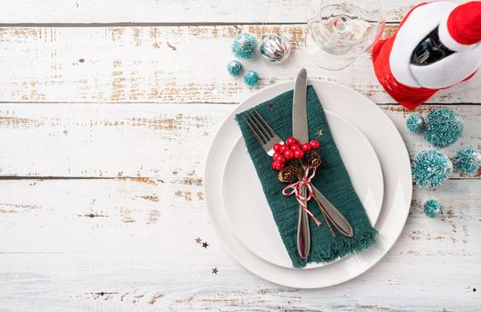 Christmas table setting with white dishware, silverware and red and green decorations on white wooden background. Top view, flat lay