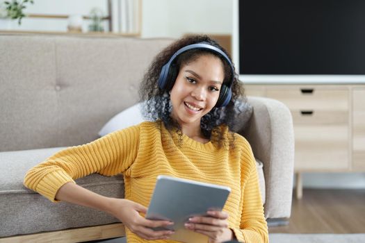Portrait of an African American with headphones and tablet smiling happily listen music while relaxing on the sofa at home.