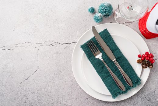 Christmas table setting with white dishware, silverware and red and green decorations on white wooden background. Top view, flat lay