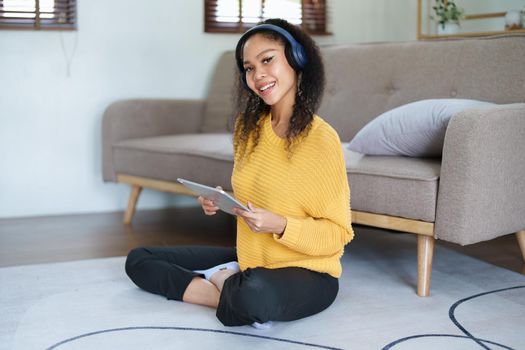 Portrait of an African American with headphones and tablet smiling happily listen music while relaxing on the sofa at home.