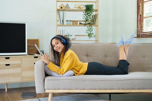 Portrait of an African American with headphones and tablet smiling happily listen music while relaxing on the sofa at home.