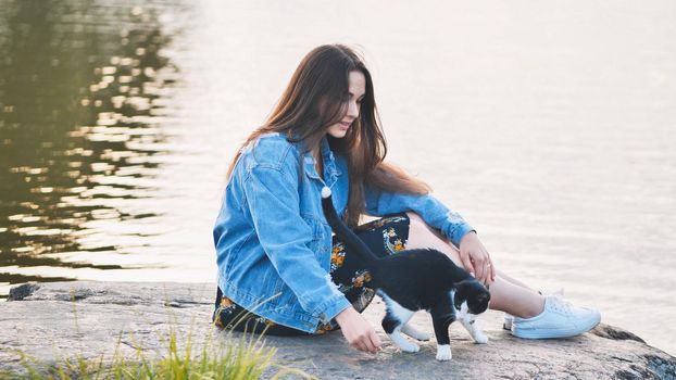 A girl plays with a cat by the lake