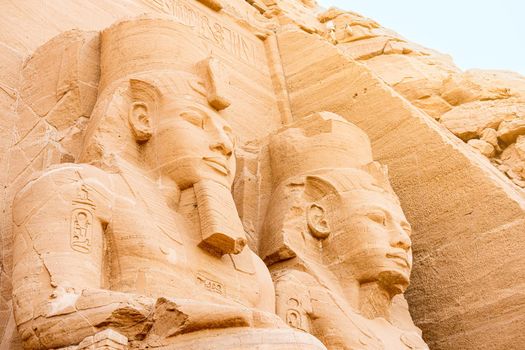 Close up of the faces of two ancient Egyptian statues in the entrance of a temple in Abu Simbel