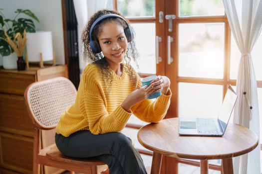 Portrait of an African American wearing headphones holding a coffee cup and using a computer.