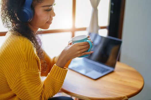 Portrait of an African American wearing headphones holding a coffee cup and using a computer.