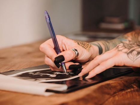 Tattoo artist drawing illustration of skull inside ink studio. Woman with black nails and rings at work. New fashion lifestyle artistic trends concept . Warm cinematic filter.