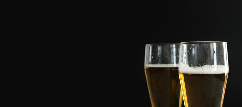 Two frosty glasses of cold golden beer with bubbles on the black background. Free space for text, copy space, banner. Drinking alcohol on party, holidays, Oktoberfest or St. Patrick's Day