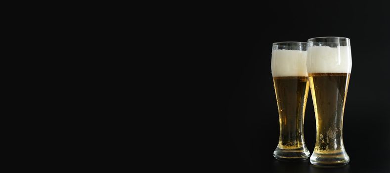 Two frosty glasses of cold golden beer with bubbles on the black background. Free space for text, copy space, banner. Drinking alcohol on party, holidays, Oktoberfest or St. Patrick's Day