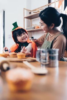 Young girl and mother at Halloween making treats and cupcake on table. Happy Halloween day.