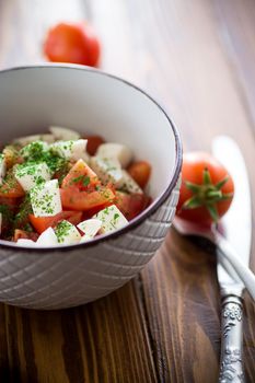 salad of fresh ripe tomatoes with mozzarella and spices in a bowl on a wooden table