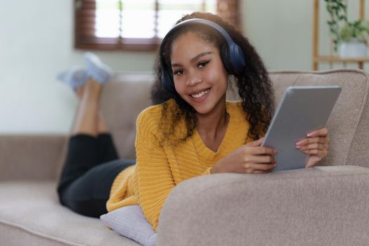 Attractive smiling young woman using tablet and listen music on sofa at home. lifestyle concept.