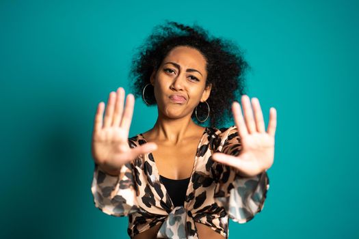 Mixed race woman disapproving with NO hand sign gesture. Denying, rejecting, disagree, portrait of beautiful girl on blue background. High quality photo