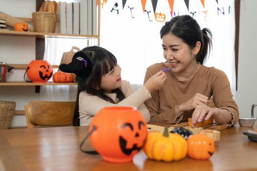 Happy smiling family mother and daughter making Halloween home decorations together while sitting at wooden table