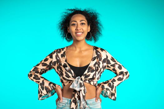 Pretty african woman with afro hair in leopard top smiling to camera over blue wall background. Cute mixed race girl's portrait. High quality photo