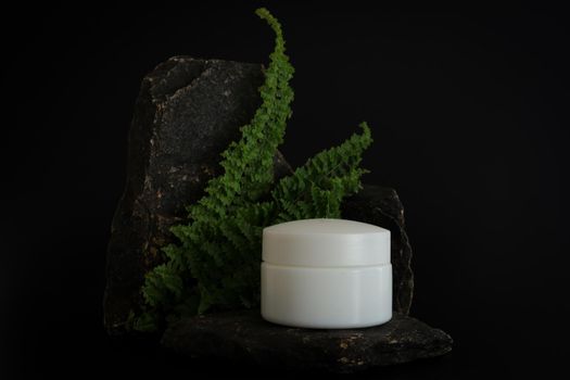 Unbranded natural cosmetic cream packaging standing on stone podium. Cream presentation on the black background. Mockup. Trending concept in natural materials. Natural cosmetic, skincare