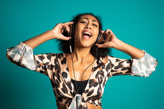 Beautiful african american woman with afro hair and big headphones having fun smiling and dancing in studio against blue background. High quality photo