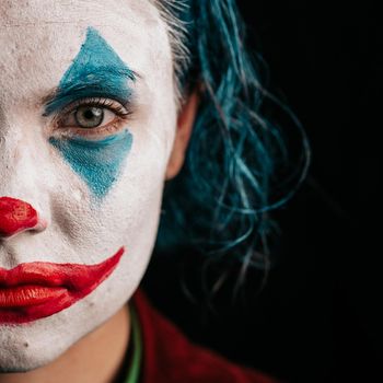 Make-up Joker with green hair for Halloween. Close-up half face on black background. Cosplay for Halloween holiday. High quality photo