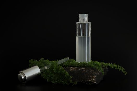 Unbranded natural cosmetic serum packaging standing on stone podium. Serum presentation on the black background. Mockup. Trending concept in natural materials. Natural cosmetic, skincare