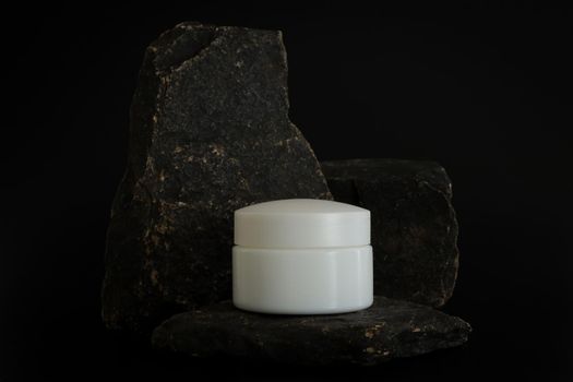 Unbranded natural cosmetic cream packaging standing on stone podium. Cream presentation on the black background. Mockup. Trending concept in natural materials. Natural cosmetic, skincare