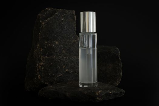 Unbranded natural cosmetic serum packaging standing on stone podium. Serum presentation on the black background. Mockup. Trending concept in natural materials. Natural cosmetic, skincare