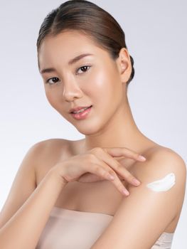 Gorgeous girl with soft makeup applying moisturizing skincare cream on shoulder isolated over white background. Skincare cream applied by female model concept.