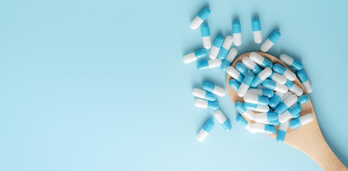 Top view of blue-white antibiotic capsule pills on wooden spoon and blue background. Antibiotic drug resistance. Prescription drug. Medical care. Pharmaceutical care. Antimicrobial drug overuse.