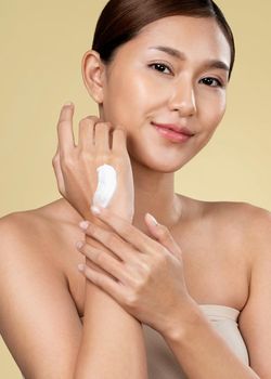 Closeup ardent girl with soft makeup looking at camera, applying moisturizing skincare cream on her hand, isolated background. Skincare cream applied by female model concept.