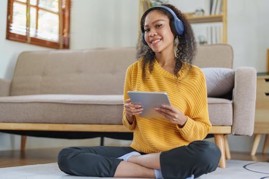 Portrait of an African American with headphones and tablet smiling happily listen music while relaxing on the sofa at home.