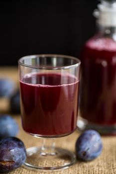plum red wine in a glass and a decanter against the background of ripe large plums on the table.
