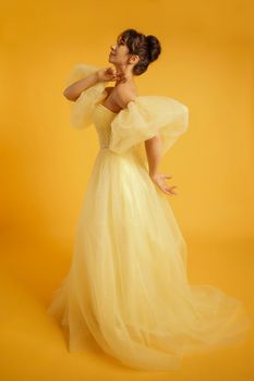 Portrait of a beautiful middle-aged woman in a yellow dress, her hair pulled up against a yellow background.