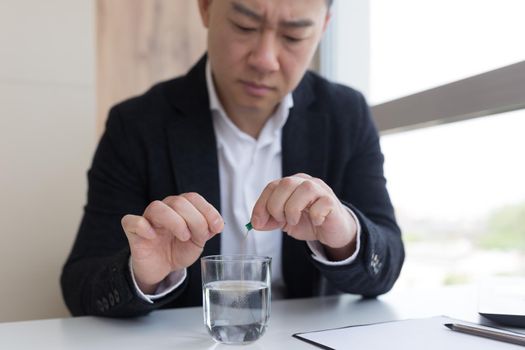 Close up of businessman in the office holding pills and glass of fresh water, taking medicine for headache, abdominal pain or taking vitamins, healthcare concept